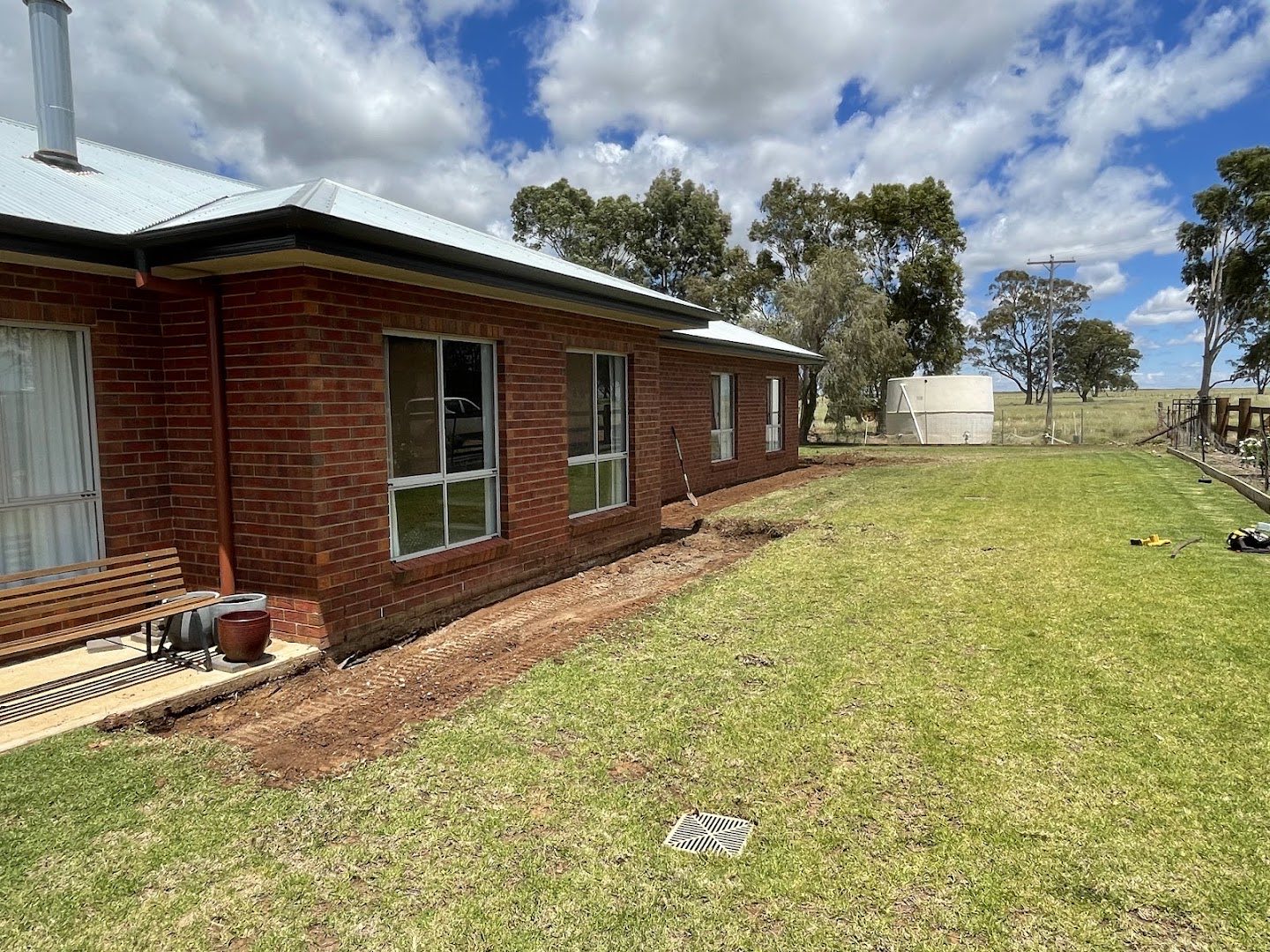 A brick homestead with a fresh trench line running along the lawn