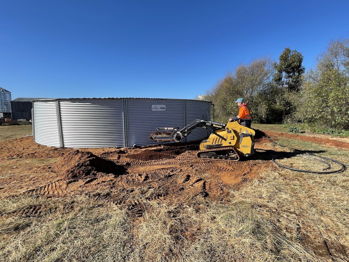 A tracked loader working beside a large steel tank on red soil