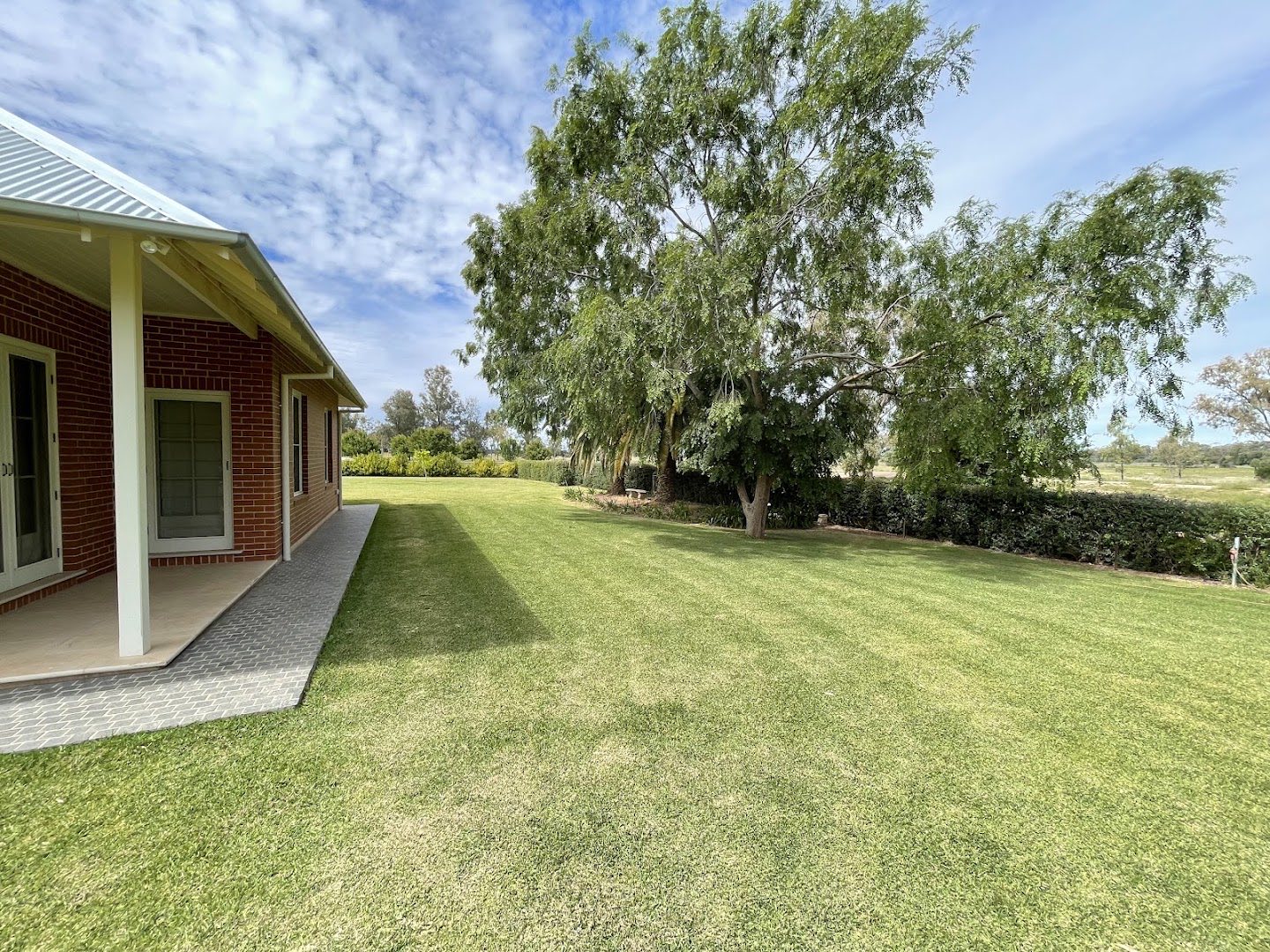 A brick house behind a wide green lawn and gum trees