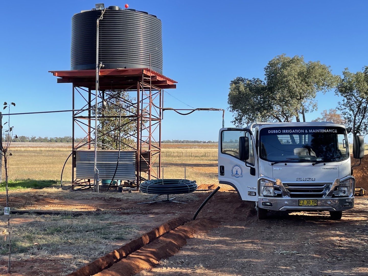 A branded truck parked beside a raised water tank stand and a fresh trench