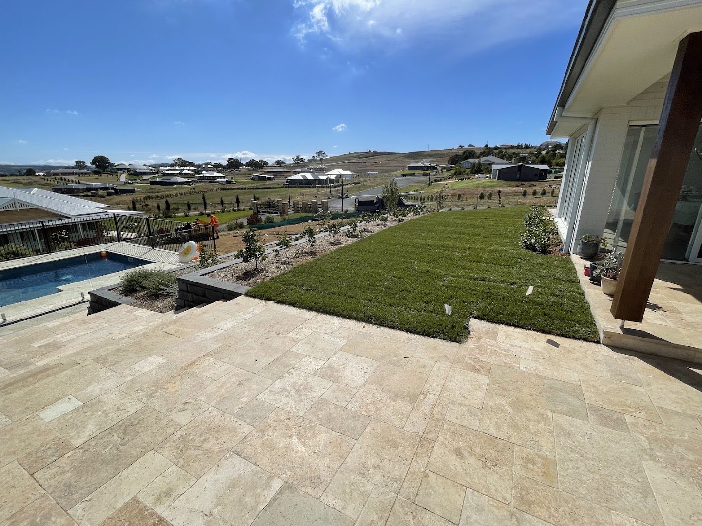 A paved terrace and swimming pool looking out over freshly laid turf