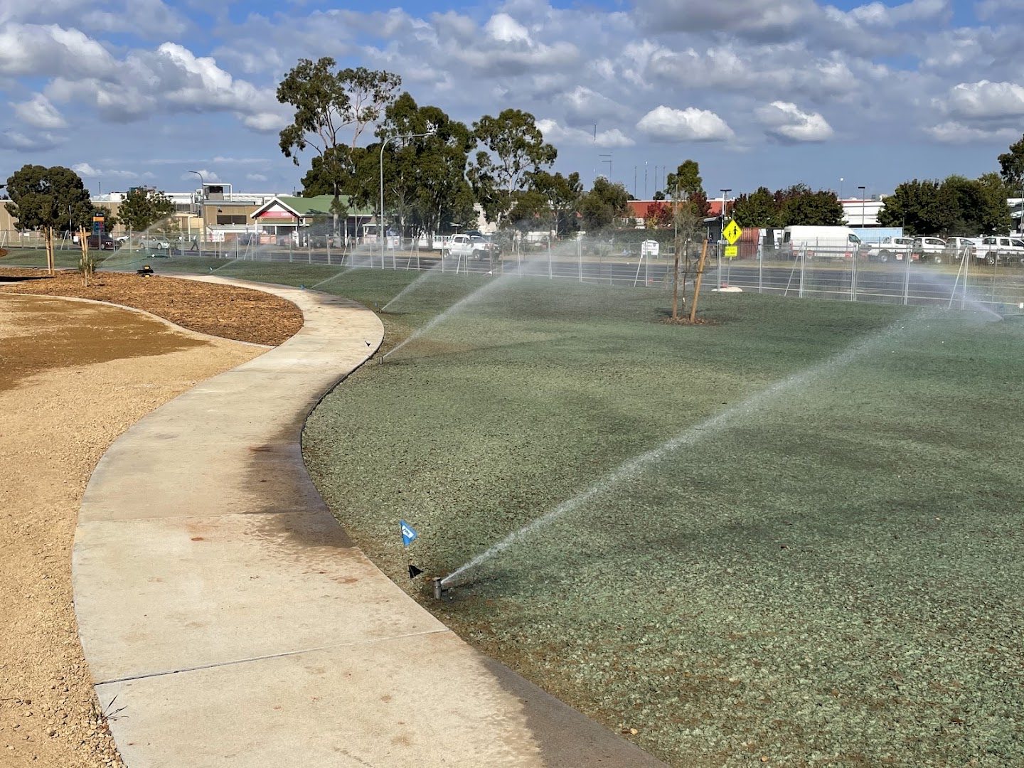 Sprinklers running across a wide green lawn beside a curved concrete path