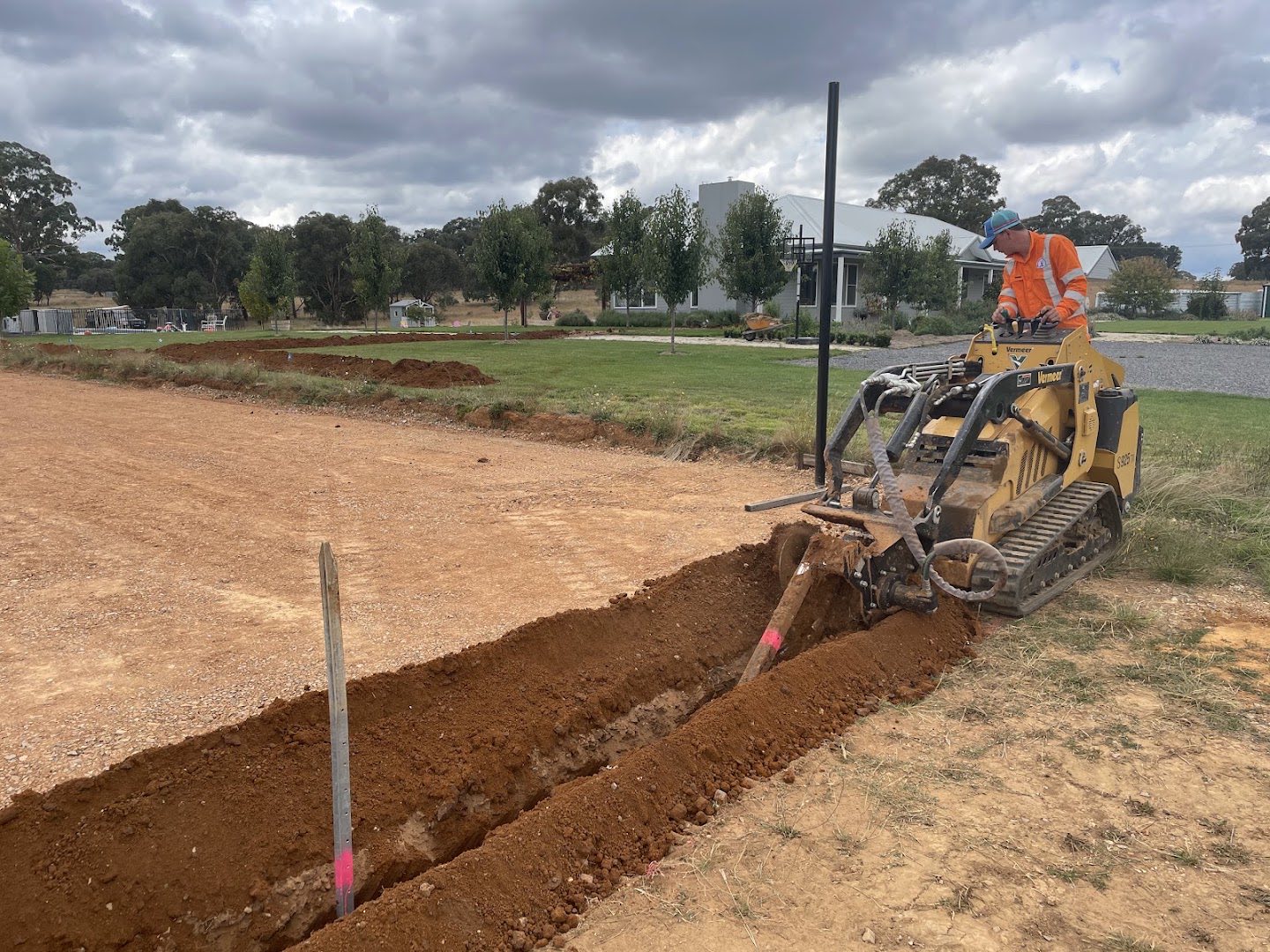 A tracked trencher cutting a long trench through red soil
