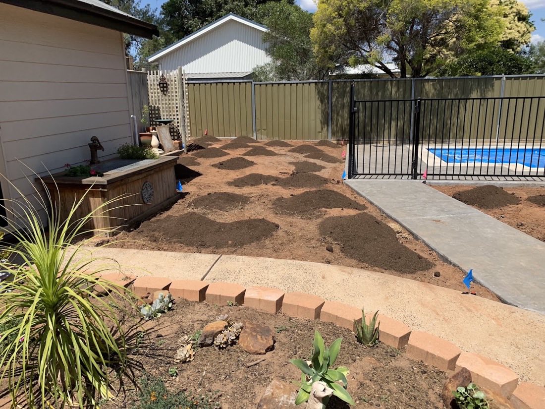 Mulched garden beds and a brick edge beside a pool fence