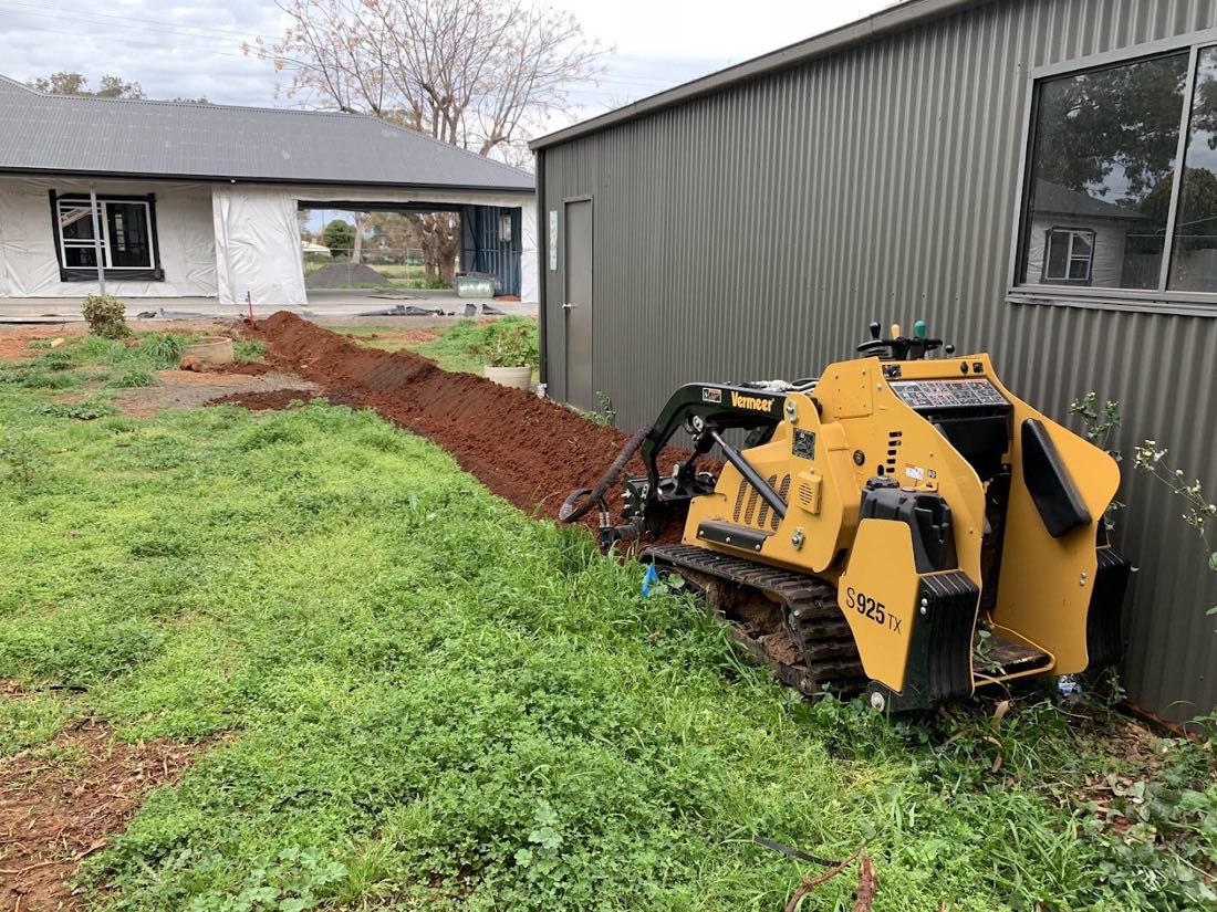 A tracked mini loader cutting a trench along the edge of a green lawn