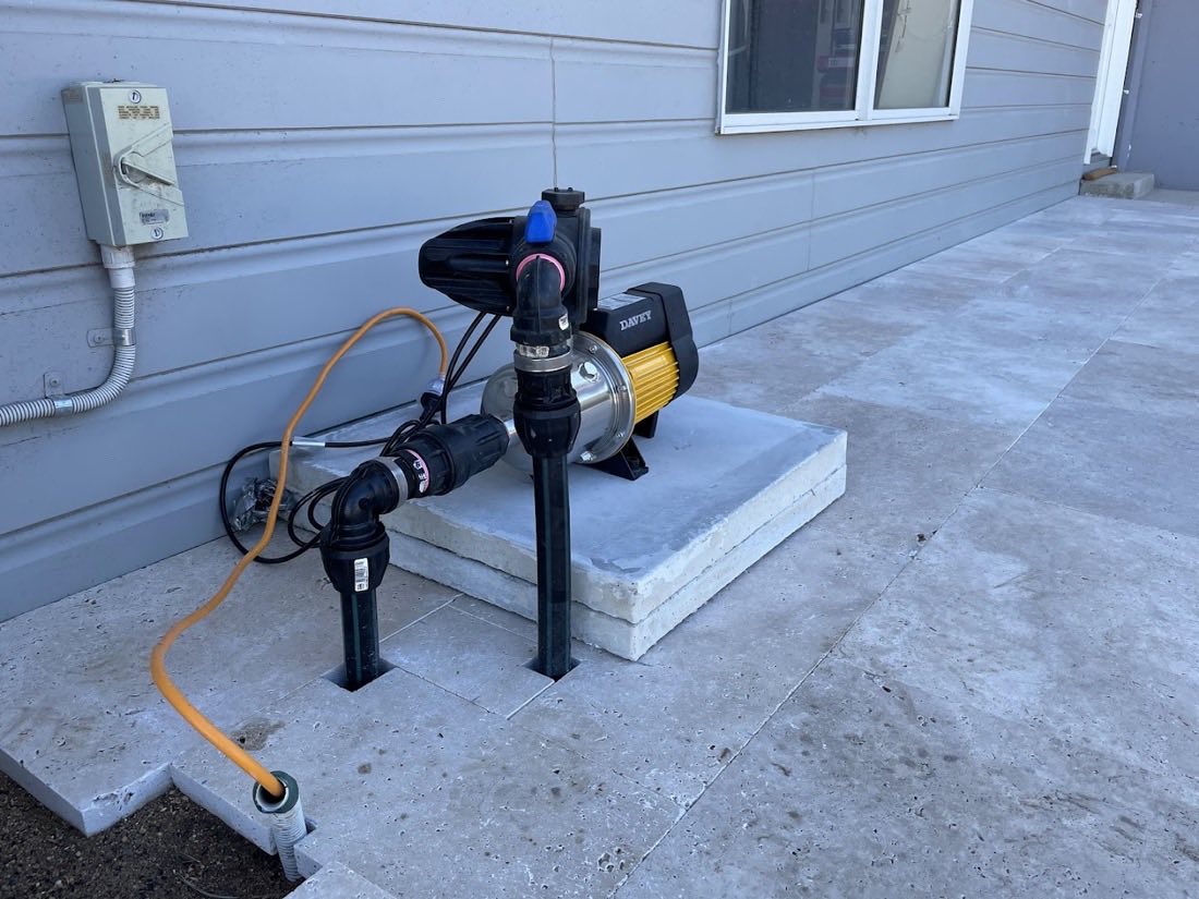 A pump mounted on a concrete slab against the wall of a house