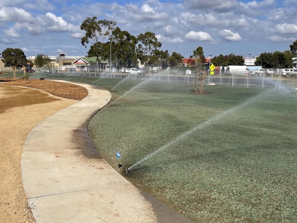 Sprinklers running across a wide green lawn beside a curved concrete path