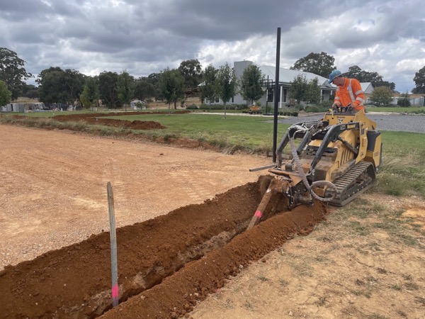 A tracked trencher cutting a long trench through red soil