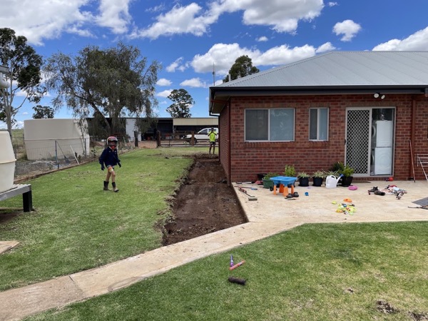 A narrow trench dug across a lawn in front of a brick house