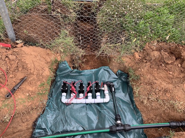 Irrigation valves laid out on green sheeting in an open trench