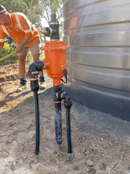 A worker fitting a filter housing to pipework beside a large water tank