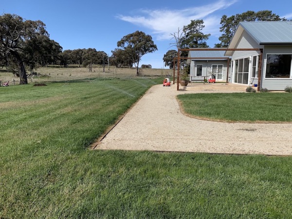 A gravel driveway running up to a country house across a mown lawn