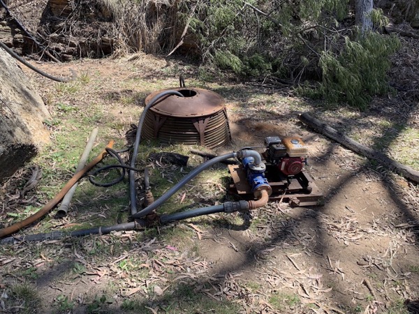 A pump and pipework set up on the ground in dappled shade