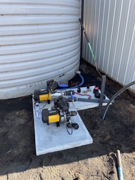 A pump and control gear mounted on a concrete pad beside a steel tank