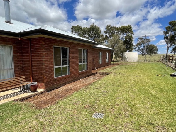 A brick homestead with a fresh trench line running along the lawn
