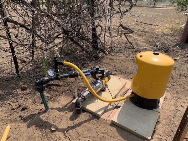 A yellow pressure tank and pump mounted on a board in bushland