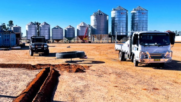Grain silos and trucks behind a fresh trench in red soil