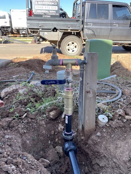 A galvanised riser and valve fitted beside a fresh trench