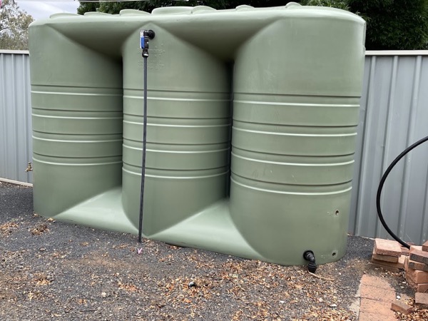 Three green poly water tanks lined up along a fence