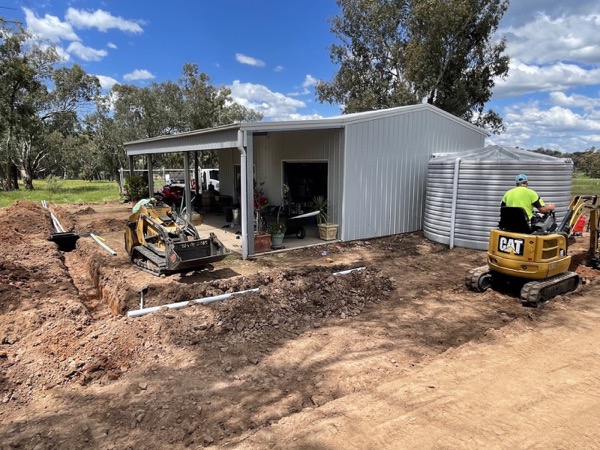 An excavator working beside a farm shed on red soil