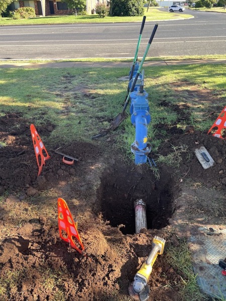 A trench dug beside a road with marker flags and pipe in place