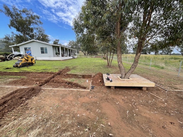 An excavator and trench work beside a house under a large gum tree