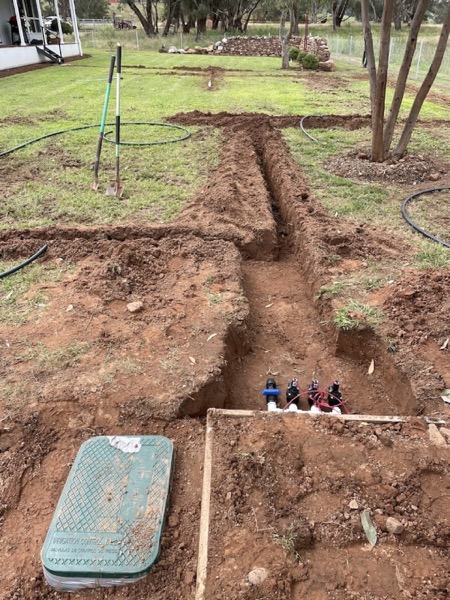 A trench dug through a grassed yard with valves set in place