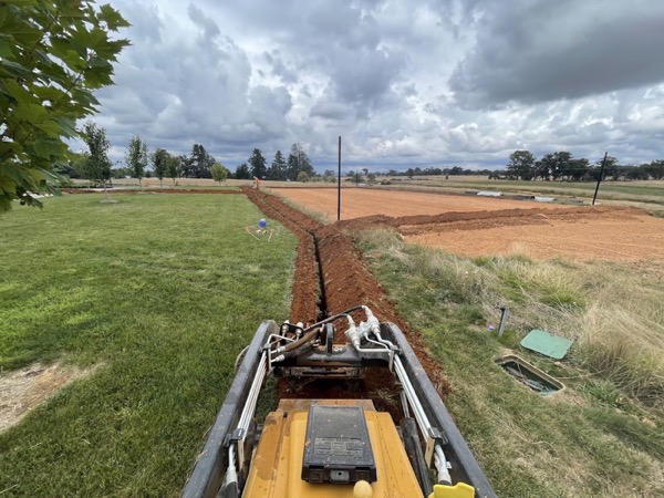 A trencher cutting a line across a lawn towards open paddocks