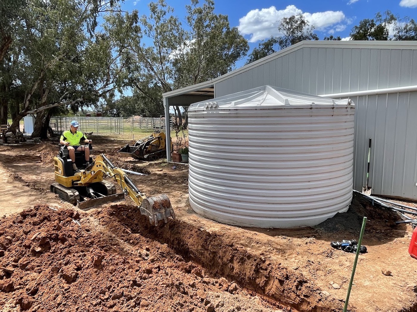 An excavator digging a trench beside a large round water tank