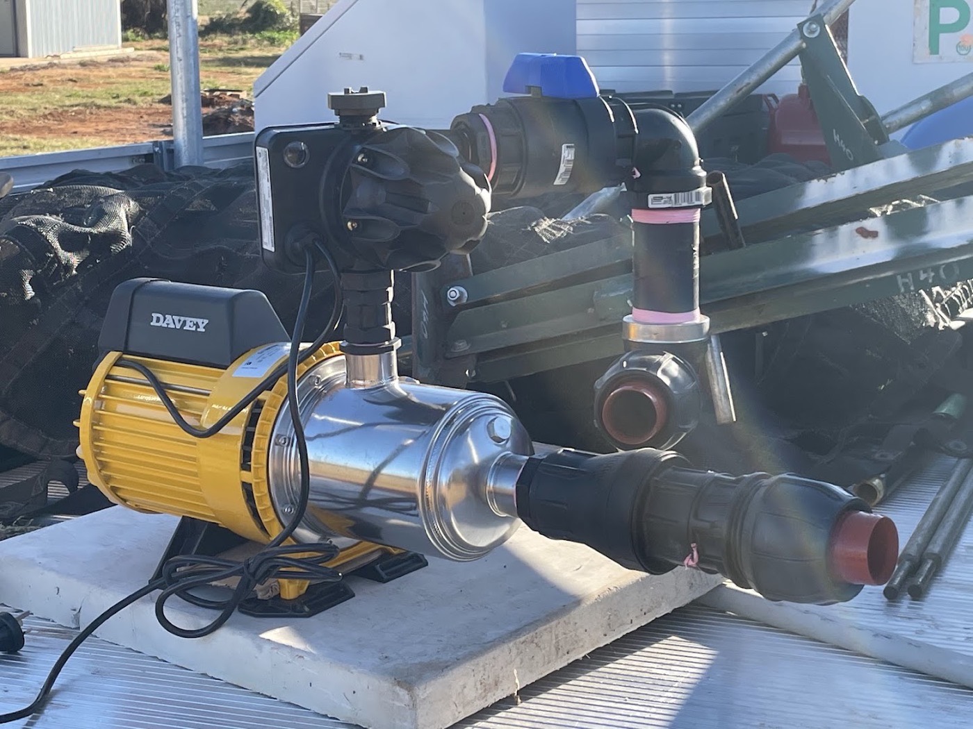 A stainless steel pump connected to blue and black pipework on a concrete pad