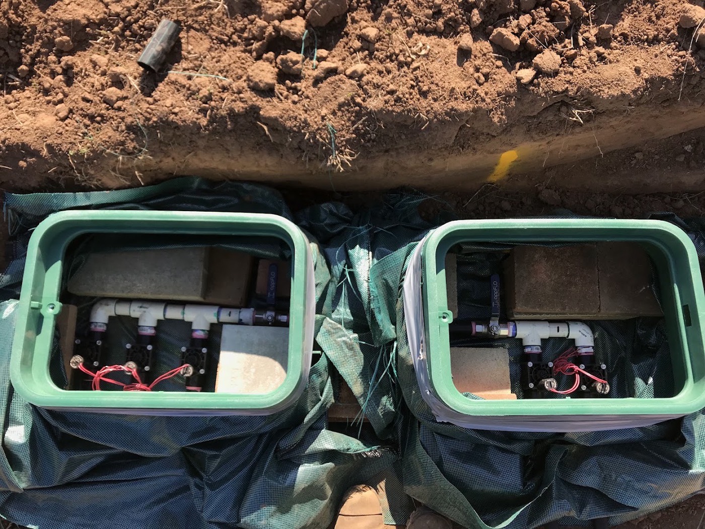 Two green valve boxes set into a trench, wired and connected