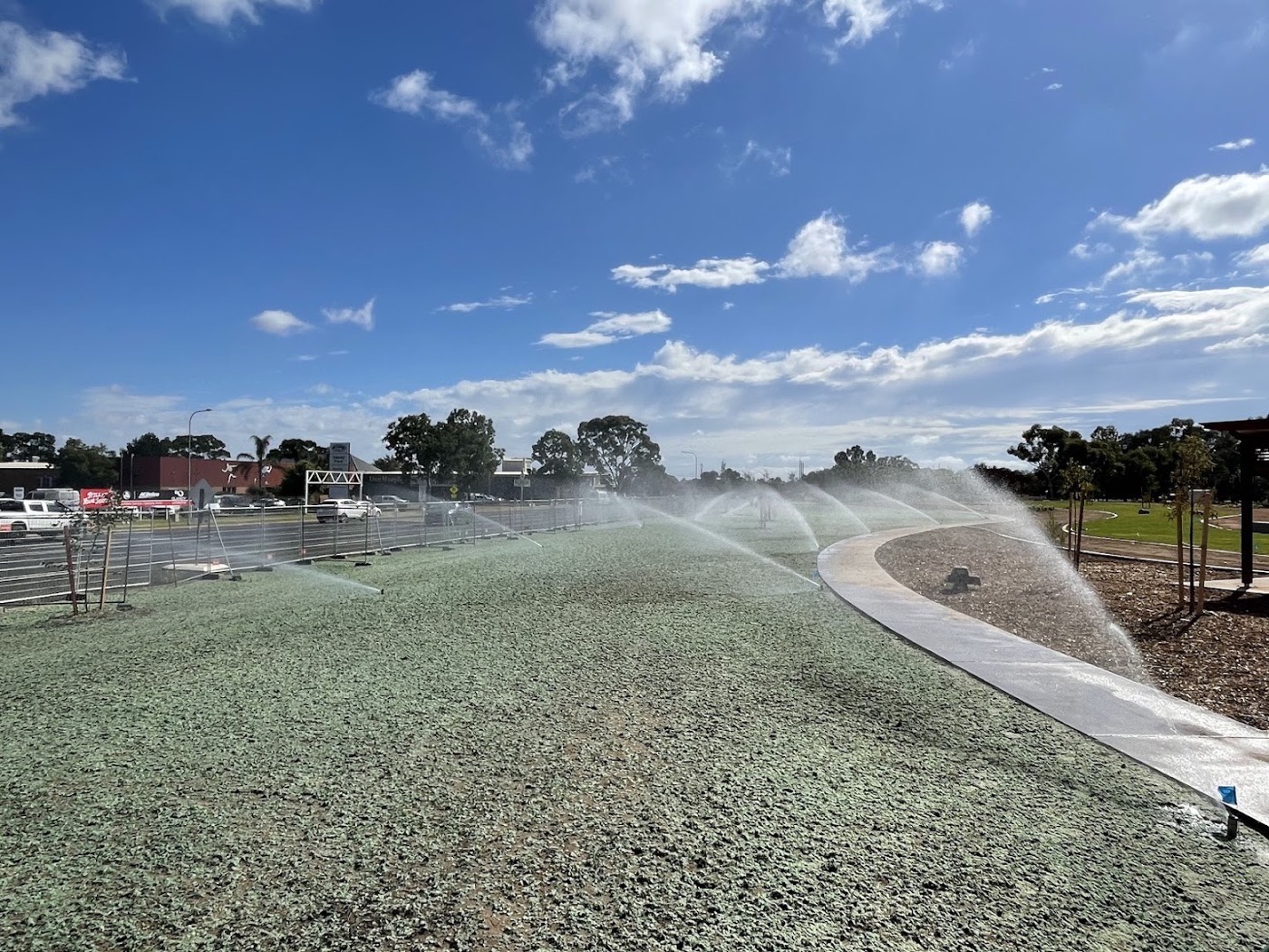 Sprinklers running across a green slope beside a concrete path